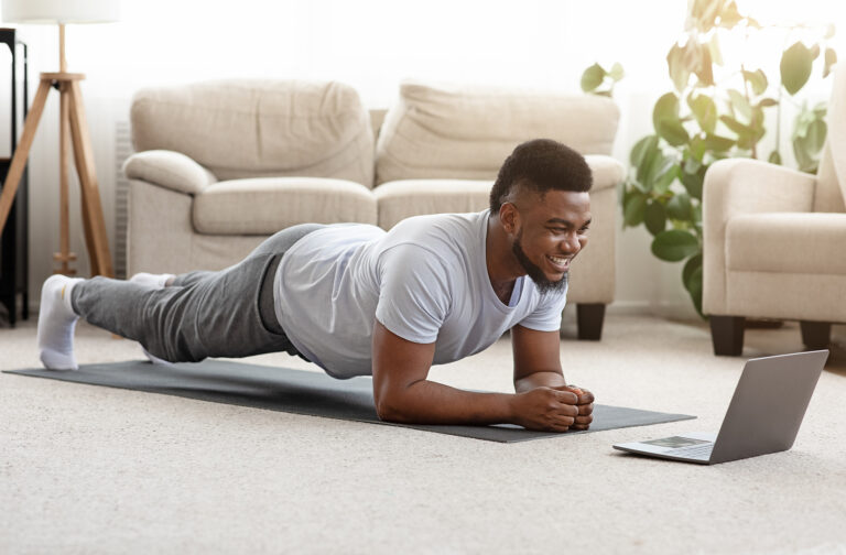 Sporty man doing yoga plank while watching online tutorial on laptop